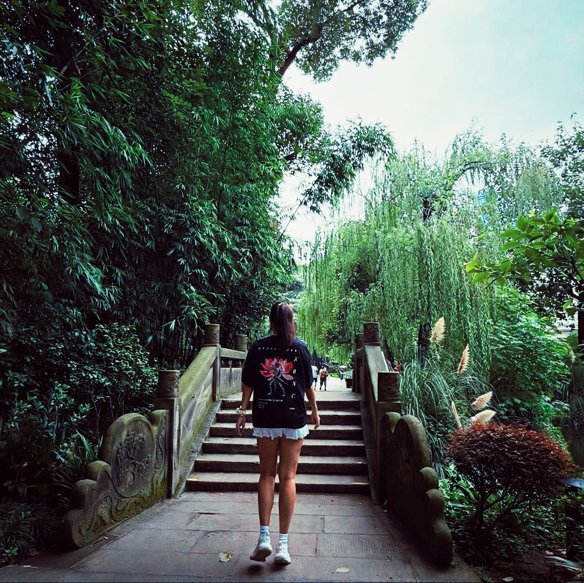 Model wearing the KONG Origin Tee walking through a garden, back view
