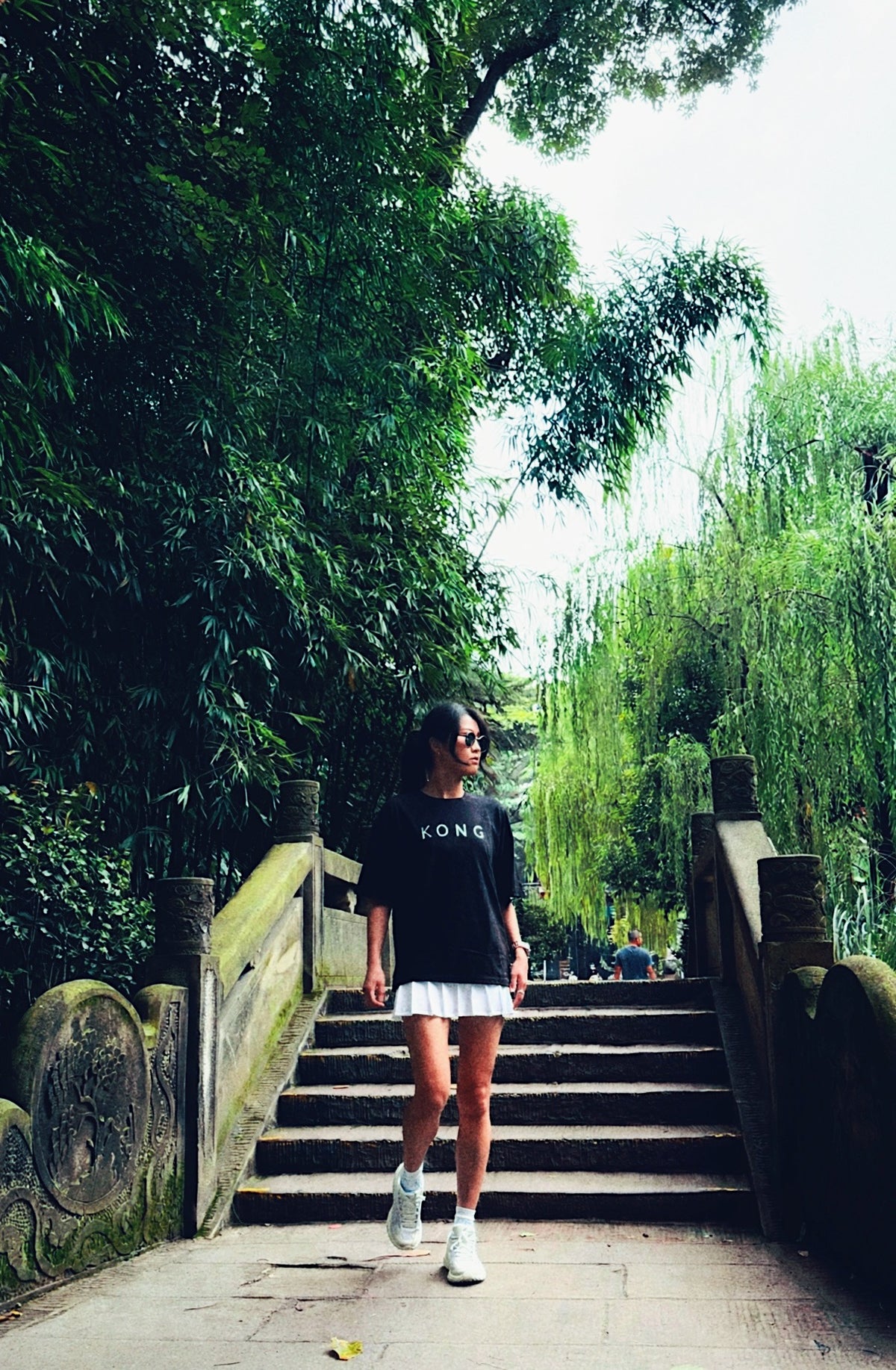 Model wearing the KONG Origin Tee on garden steps, back graphic visible