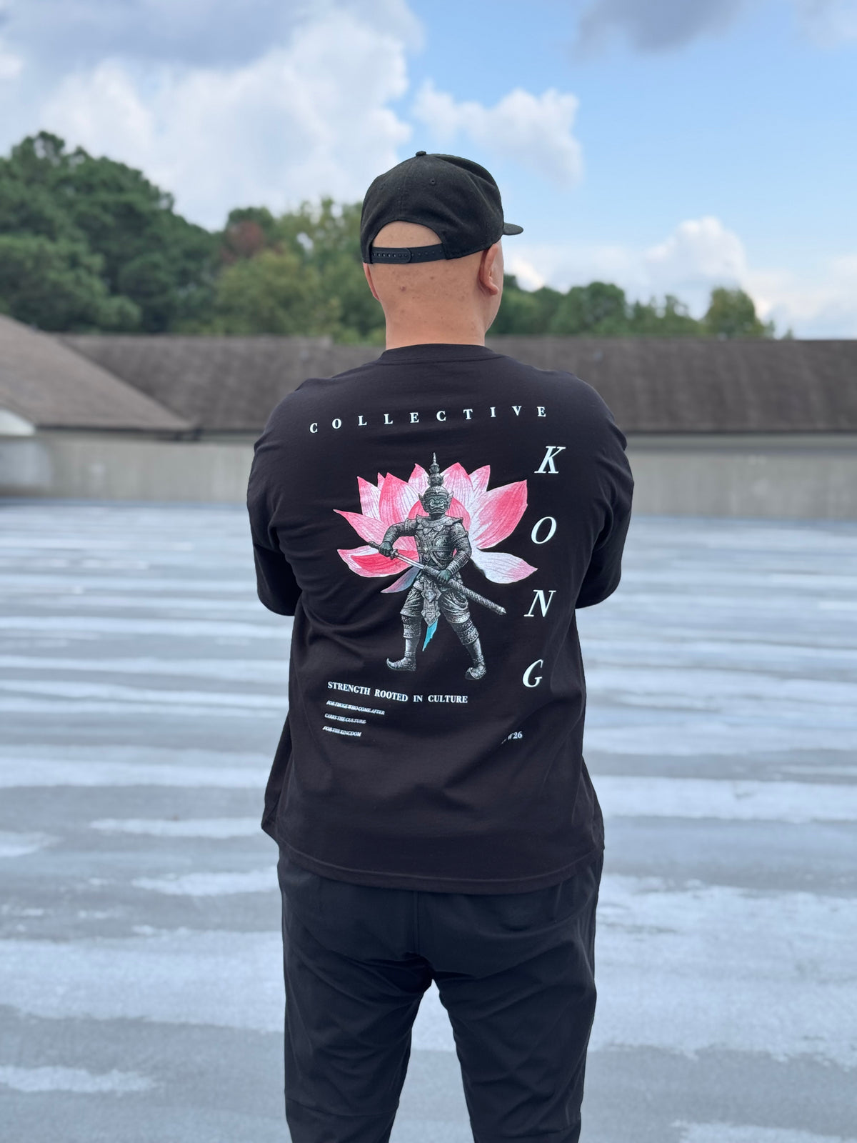 Model wearing the KONG Origin Tee on a rooftop, back view showing Yaksha and lotus graphic